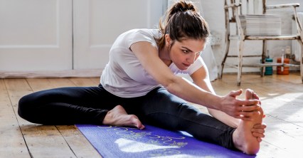Young woman practicing yoga, touching toes in apartment